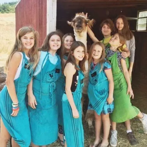 Group of teens in The Kitchen at Middleground Farms aprons taking a picture with a llama