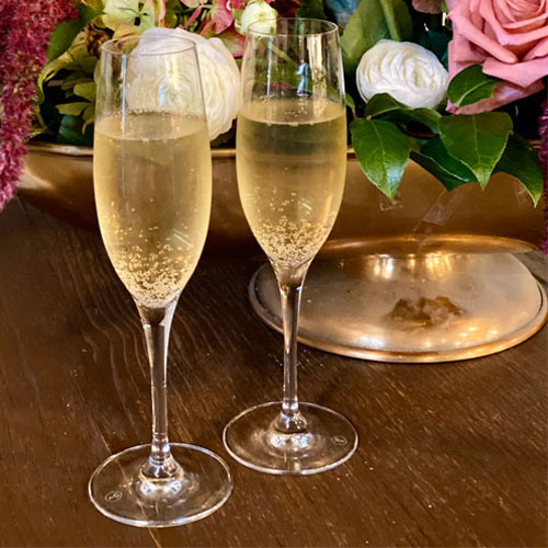 Two glasses of champagne with a bouquet of roses in the background